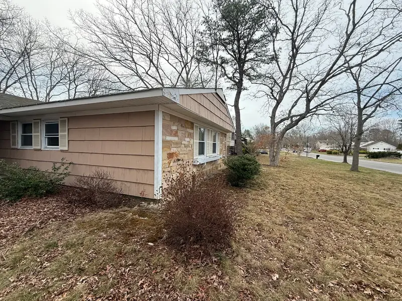 Shingled ranch with stone trim and bare shrubs, Coram, NY